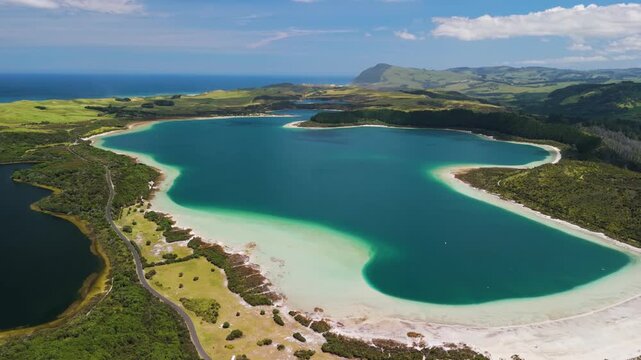 Fast wide angle orbital shot revealing dramatic contrast between twin freshwater lakes connected by narrow isthmus with white sand beaches and ocean beyond