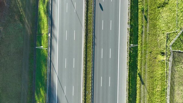 Top‑down aerial view of two parallel highway lanes with moving cars and grassy edges in bright daylight.