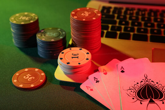 Laptop with playing cards and poker chips on green table, closeup