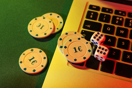 Laptop with poker chips and dices on green table, closeup