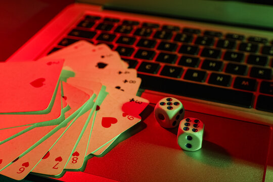 Laptop with playing cards and dices on table in casino, closeup