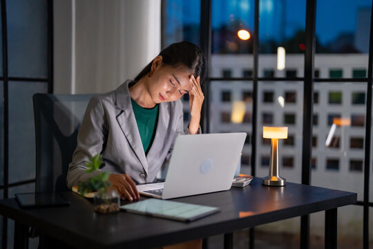Alone Working Late at Night. Asian business woman at workplace in office late night work at a desk in a dark office working on a laptop late in the evening.