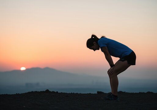 Female athlete resting after intense run at sunset, hands on knees