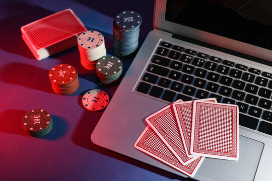 Laptop with poker chips and playing cards on table in casino, closeup