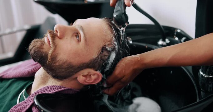 Man, relax and washing hair in salon with water for maintenance, hygiene and styling appointment. People, hairstylist or clean client scalp in small business with liquid soap, massage and treatment.
