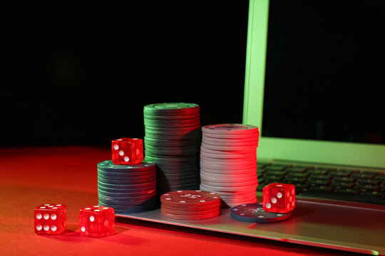 Laptop with poker chips and dices on red table in casino, closeup