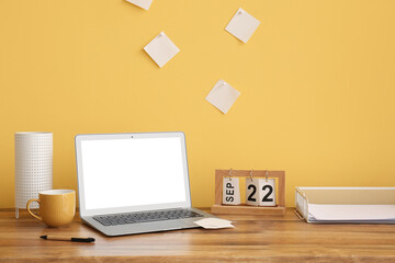 Modern laptop, calendar, paper sheets and cup of coffee on wooden table near color wall