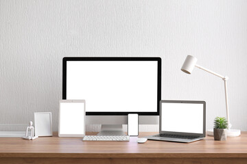 Set of modern gadgets, blank picture frame and decor on table near light wall