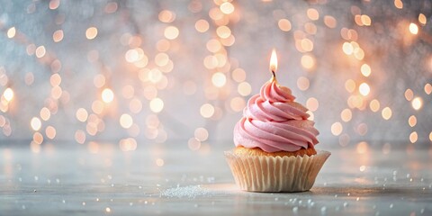 A single pink frosted cupcake with a lit candle, resting on a wood surface against a bokeh background of warm lights.