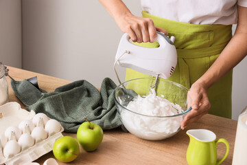 Woman whipping egg albumen with mixer at table in kitchen