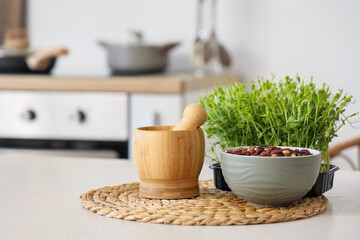 Wooden mortar with pestle, sprouts and red beans on table in kitchen