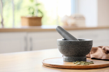 Granite mortar with pestle and pumpkin seeds on table in kitchen, closeup
