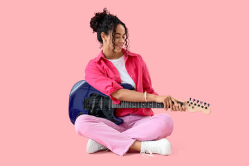 Pretty young African-American woman with electric guitar on pink background