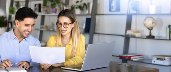 Two happy successful young Hispanic coworkers analyzing document