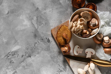 Bowl with different fresh mushrooms and knife on grey grunge background