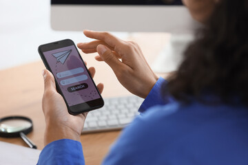 Young businesswoman using mobile phone to search for tickets online in office, closeup