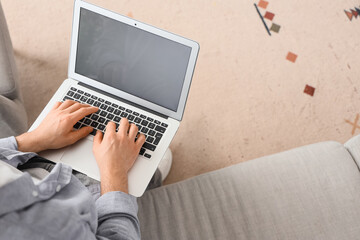 Young man using blank laptop to search online on sofa at home, top view