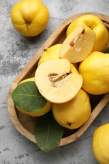 Wooden tray with sweet ripe quinces and leaves on grey background