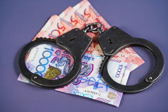 Banknotes of Kazakhstani tenge and handcuffs on a paper background. Fraud, corruption and bribery. Financial fraud. - Powered by Adobe