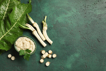 Bowl of horseradish sauce with peeled roots, slices and parsley on green grunge background