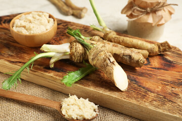 Bowl and jar of horseradish sauce with roots on light grunge background