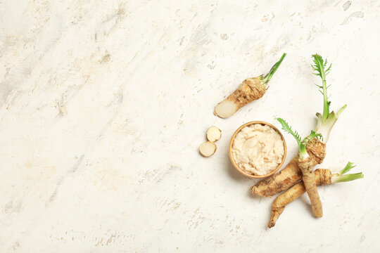 Bowl of horseradish sauce with roots and slices on light grunge background