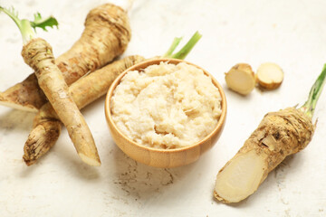 Bowl of horseradish sauce with roots and slices on light grunge background