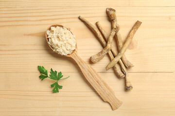 Spoon of horseradish sauce with roots and parsley on wooden background
