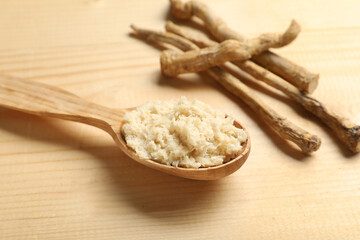 Spoon of horseradish sauce with roots on wooden background