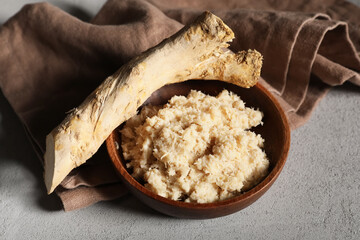 Bowl of horseradish sauce with root on grey grunge background