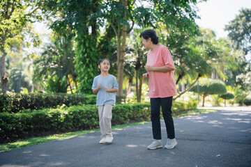 Fototapeta premium Elderly woman and young girl engaging in outdoor jogging together in a sunny park, promoting healthy lifestyle and family bonding through exercise