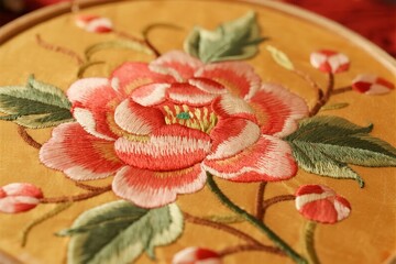 Close-up of a hand-embroidered floral design featuring a pink and red rose on golden fabric