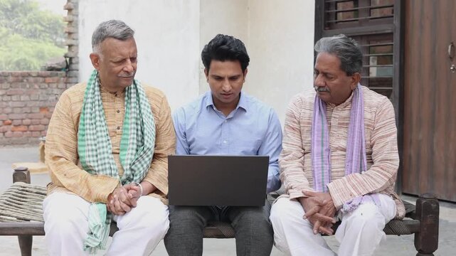 Senior rural Indian people sitting with insurance agent showing plans on laptop. Bank manger explain government loan scheme to village farmers.