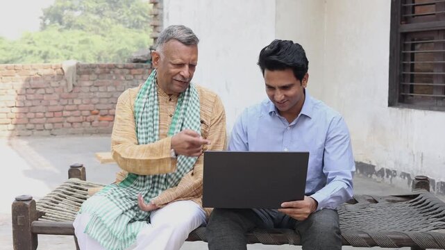 Senior rural Indian farmer sitting with insurance agent showing plans on laptop. Bank manger explain government loan scheme to village man.