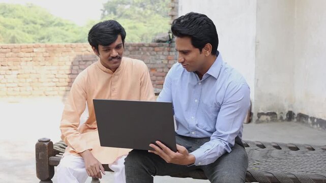 Young rural Indian man sitting with insurance agent showing plans on laptop. Bank manger explain government loan scheme to village people.