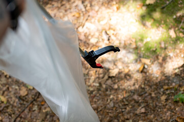 Forest cleanup in action: trash grabber tool with plastic bag in woodland setting. High quality...