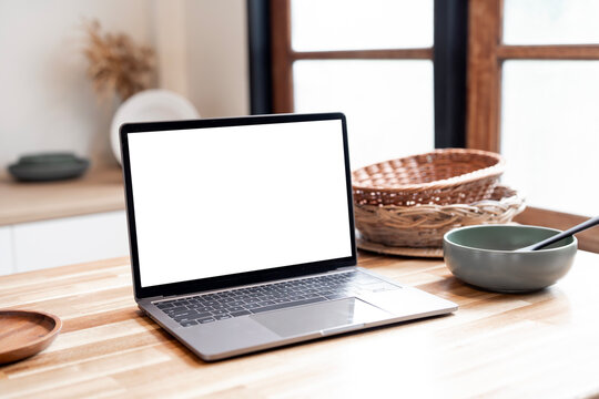 Close-up of a modern laptop with a blank white screen on a wooden kitchen counter next to a bowl of food, perfect for mockup or digital overlay. - Powered by Adobe