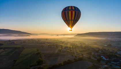 Hot air balloon soaring above misty landscape at sunrise.