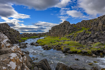 Thingvellir National Park Öxarárfoss waterfall river flowing through the mossy tectonic rift valley under blue sky in Iceland