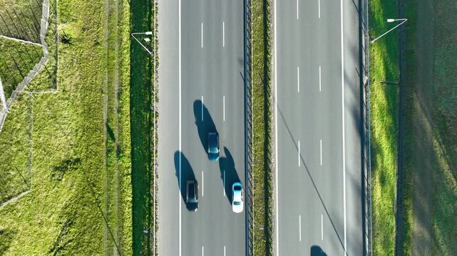 Drone top‑down view of two cars driving on parallel highway lanes with grassy median and clear markings.