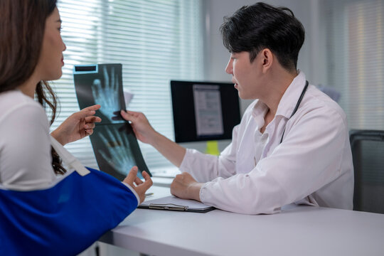 Doctor showing x-ray scan to patient with arm in sling in hospital room