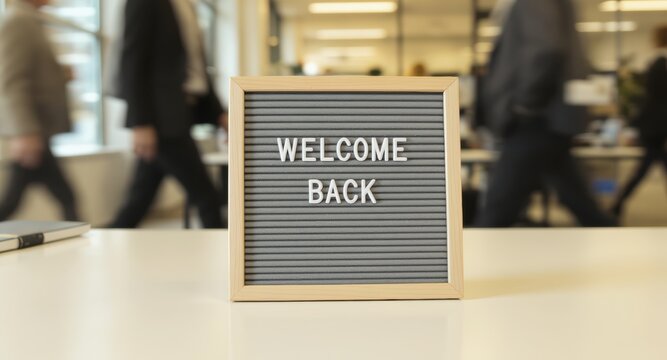 Close-up of 'Welcome Back' Letter Board Sign on Office Desk with Blurry Businesspeople Walking in Background, Return to Work and Office Reopening Concept.