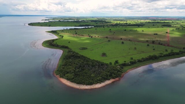 High-angle drone shot of a massive reservoir in Mato Grosso do Sul, Brazil, bordering expansive, well-maintained green farmlands and a small patch of native forest.