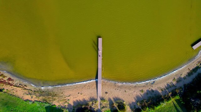 Top-down aerial shot of the jetty at Siloam Pool, highlighting the yellow water and a couple running toward the end of the jetty. Bright tones, clear patterns and a unique coastal salt pool setting.
