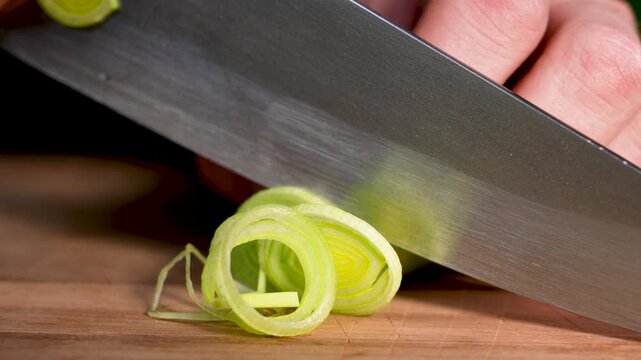 A sharp kitchen knife cuts cleanly through a fresh leek in a detailed macro close-up. The crisp green layers and smooth motion highlight precise food preparation and natural culinary visuals.