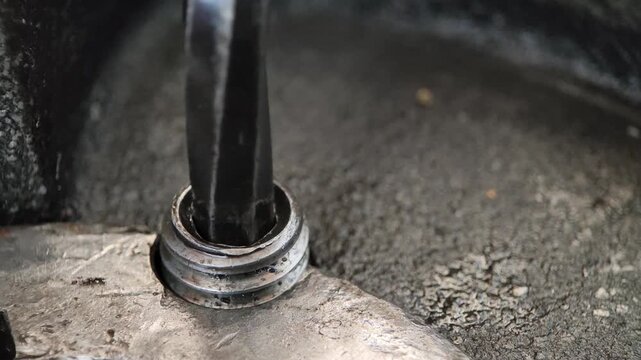 Close-up of a metal L-shaped hex key (Allen wrench) being used to tighten or loosen a hex socket bolt in a gritty, industrial, or mechanical assembly, highlighting repair work.