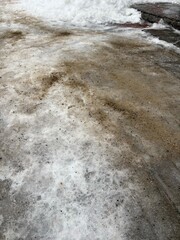 Ice-covered pavement with melting snow and rock salt in winter  