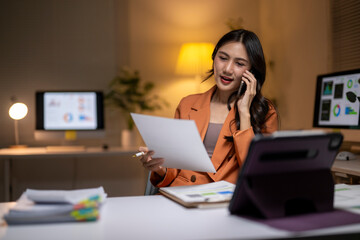 Asian businesswoman working late managing documents and phone call