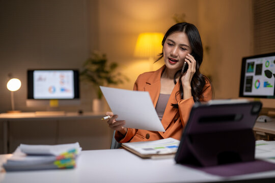 Asian businesswoman working late managing documents and phone call
