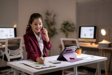 Asian businesswoman working late multitasking with phone call